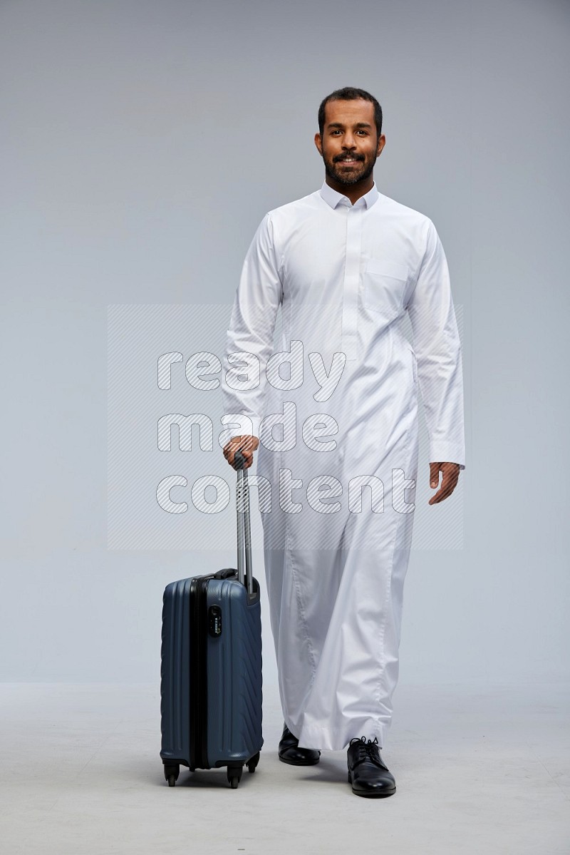 Saudi man wearing thob standing holding Travel bag on Gray background