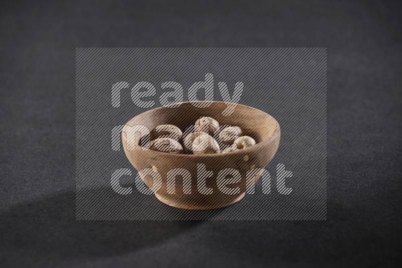 A wooden bowl full of whole nutmeg seeds on a black flooring