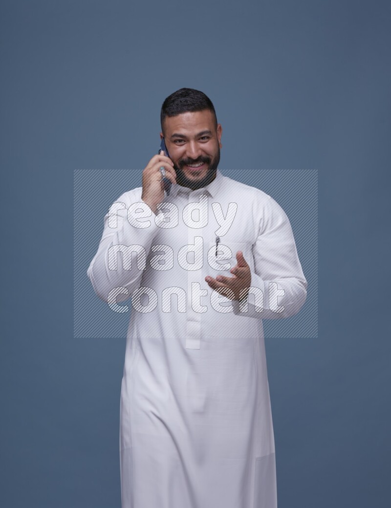 A Saudi man calling on blue background wearing Saudi Thob