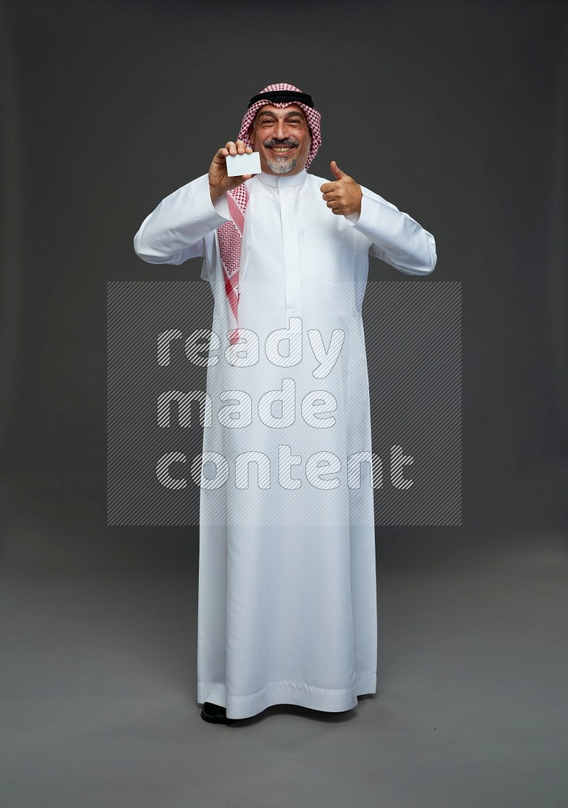 Saudi man with shomag Standing holding ATM card on gray background