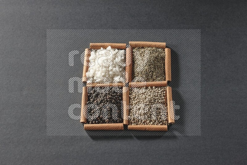 4 مربعات من عيدان القرفة ممتلئة بحبوب الفلفل الأسود والكمون وحبوب الفلفل الأبيض والملح الأبيض على أرضية سوداء