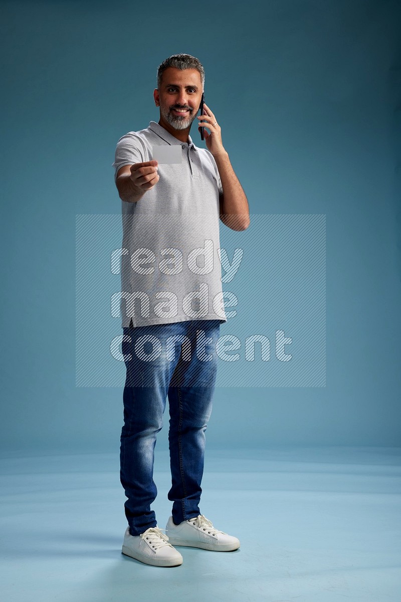 Man Standing holding ATM while talking on phone on blue background