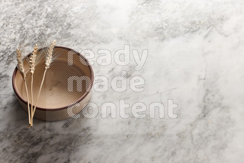 Wheat stalks on beige pottery oven bowl on grey marble background