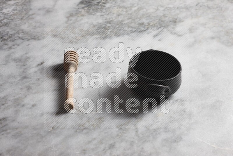 Black pottery bowl with wooden honey dipper on the side on grey marble background