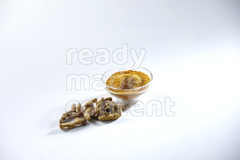 A glass bowl full of turmeric powder and dried whole fingers beneath it on white flooring