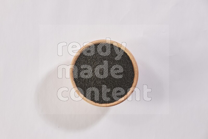 A wooden bowl full of black seeds on a white flooring