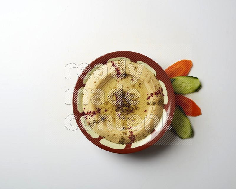 Hummus in a traditional plate garnished with zaatar & sumak on a white background