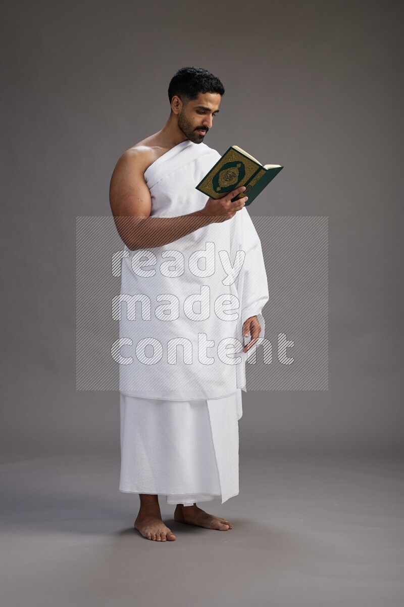 A man wearing Ehram Standing reading quran on gray background