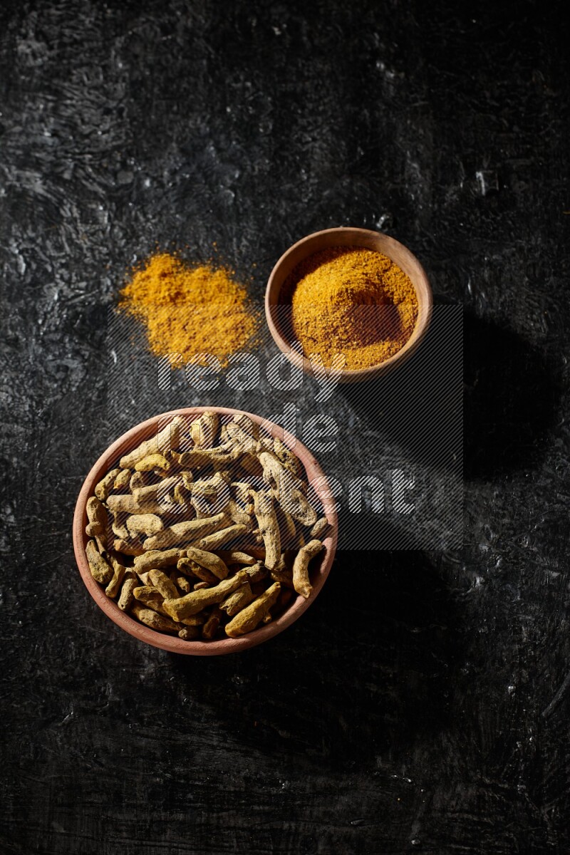 وعاءان خشبيان، أحدهما ممتلئ ببودرة الكركم والآخر بأصابع الكركم المجففة، على خلفية سوداء