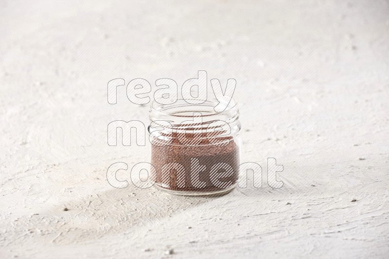 A glass jar full of garden cress seeds on a textured white flooring
