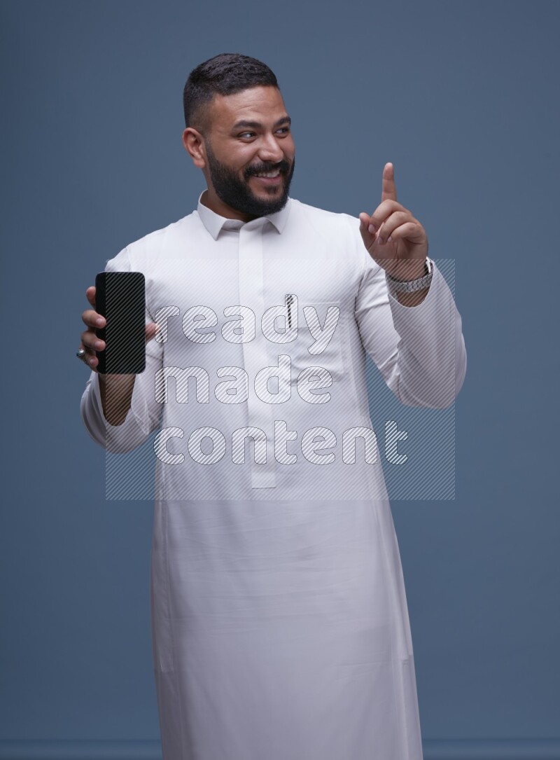 A man Showing his phone in Blue Background wearing Saudi Thob