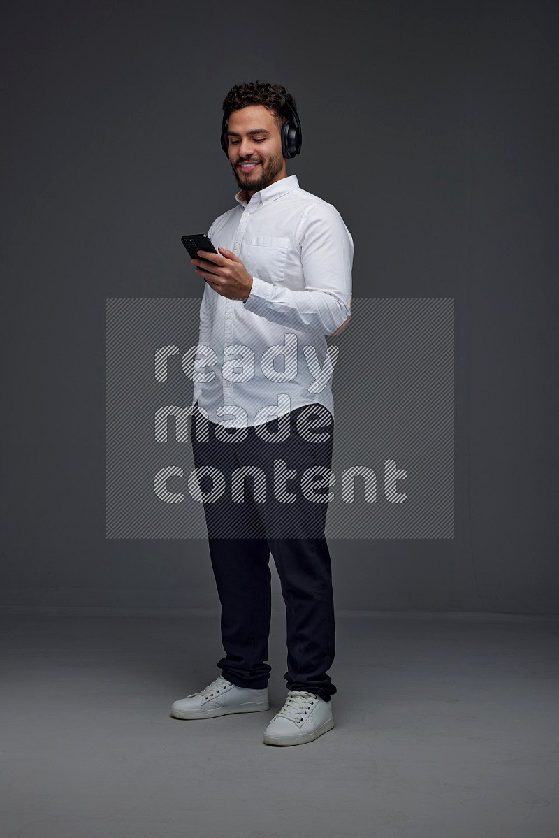 A man wearing smart casual and using his phone and headphone eye level on a gray background