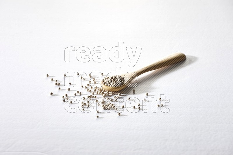 A wooden spoon full of white pepper beads on white flooring