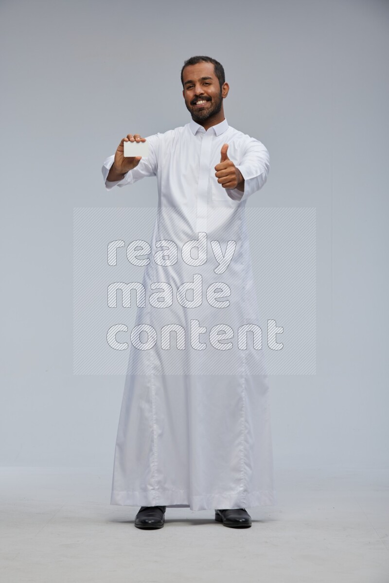Saudi man wearing Thob standing holding ATM card on Gray background