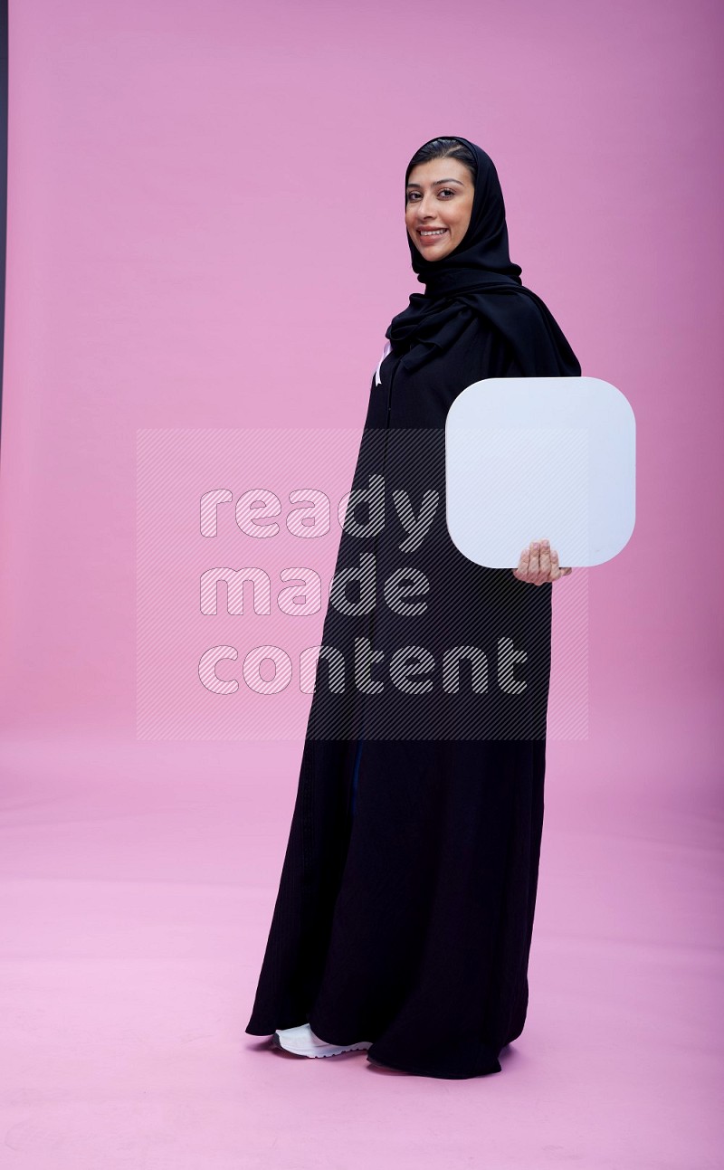 Saudi woman wearing pink ribbon on Abaya standing holding social media signs on pink background