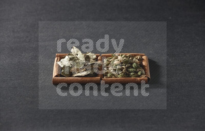 مربعان من أعواد القرفة ممتلئان بحبوب الهيل وأوراق الغار علي خلفية سوداء