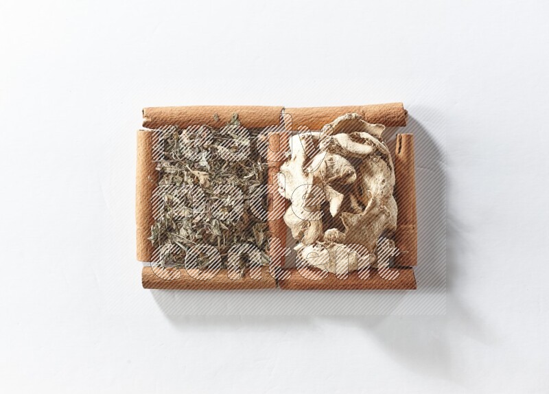 مربعان من أعواد القرفة ممتلئان بالزنجبيل المجفف والريحان المجفف علي خلفية بيضاء