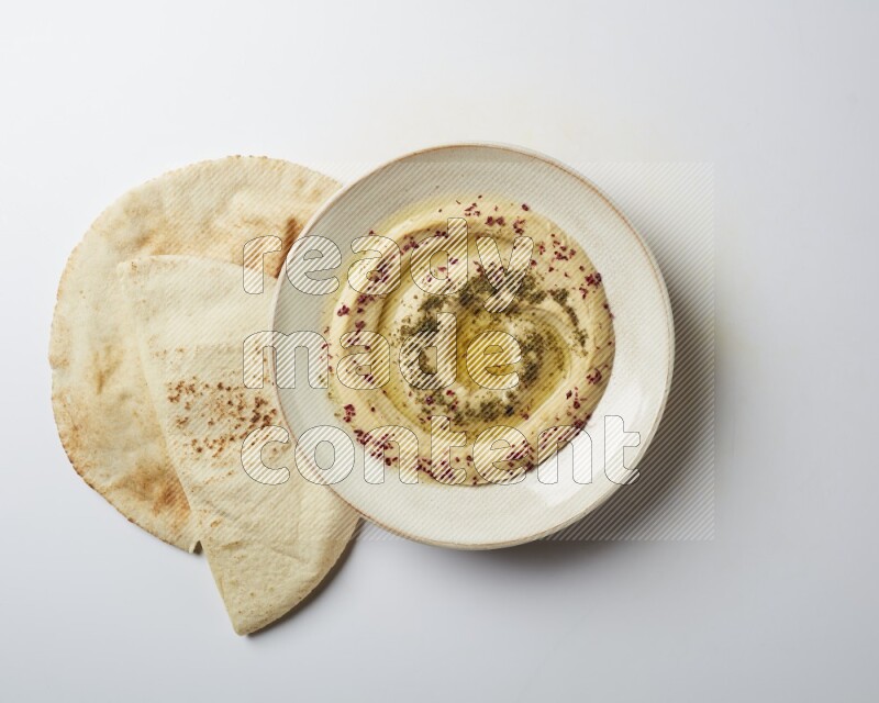 Hummus in a pottry plate garnished with zaatr & sumak on a white background