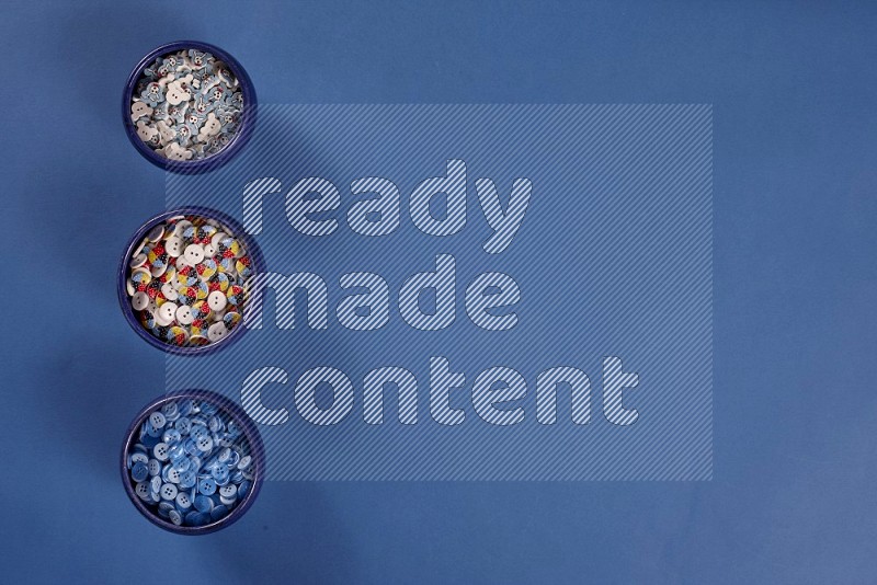 Multicolored pottery bowl full of colored buttons on blue background