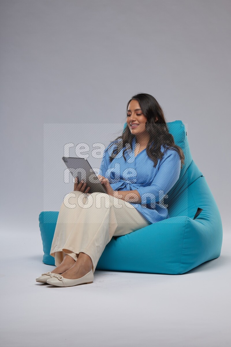 A woman sitting on a blue beanbag and working on tablet