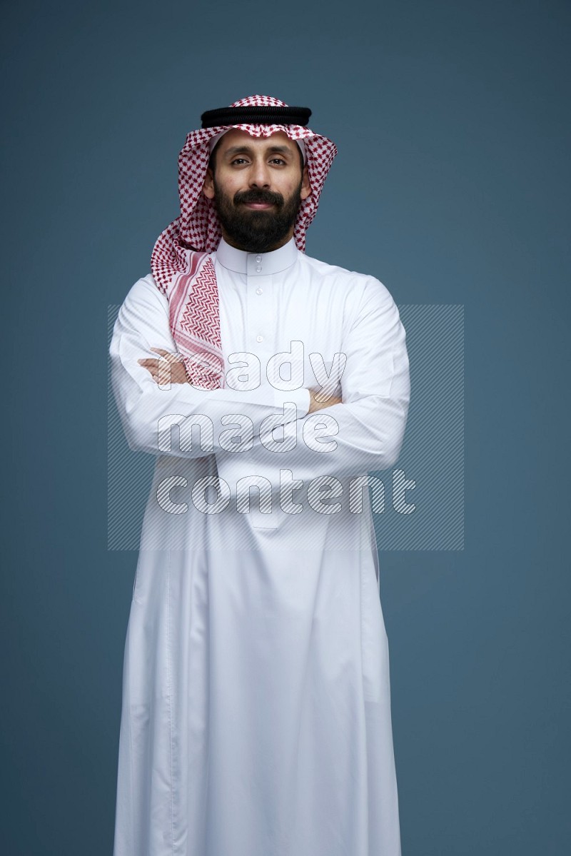 A man posing in a blue background wearing Saudi Thob and Shomag