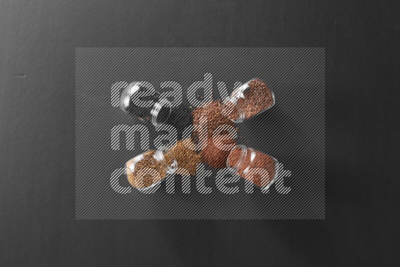 4 glass spice jars full of black seeds, mustard seeds, flax and garden cress on black flooring