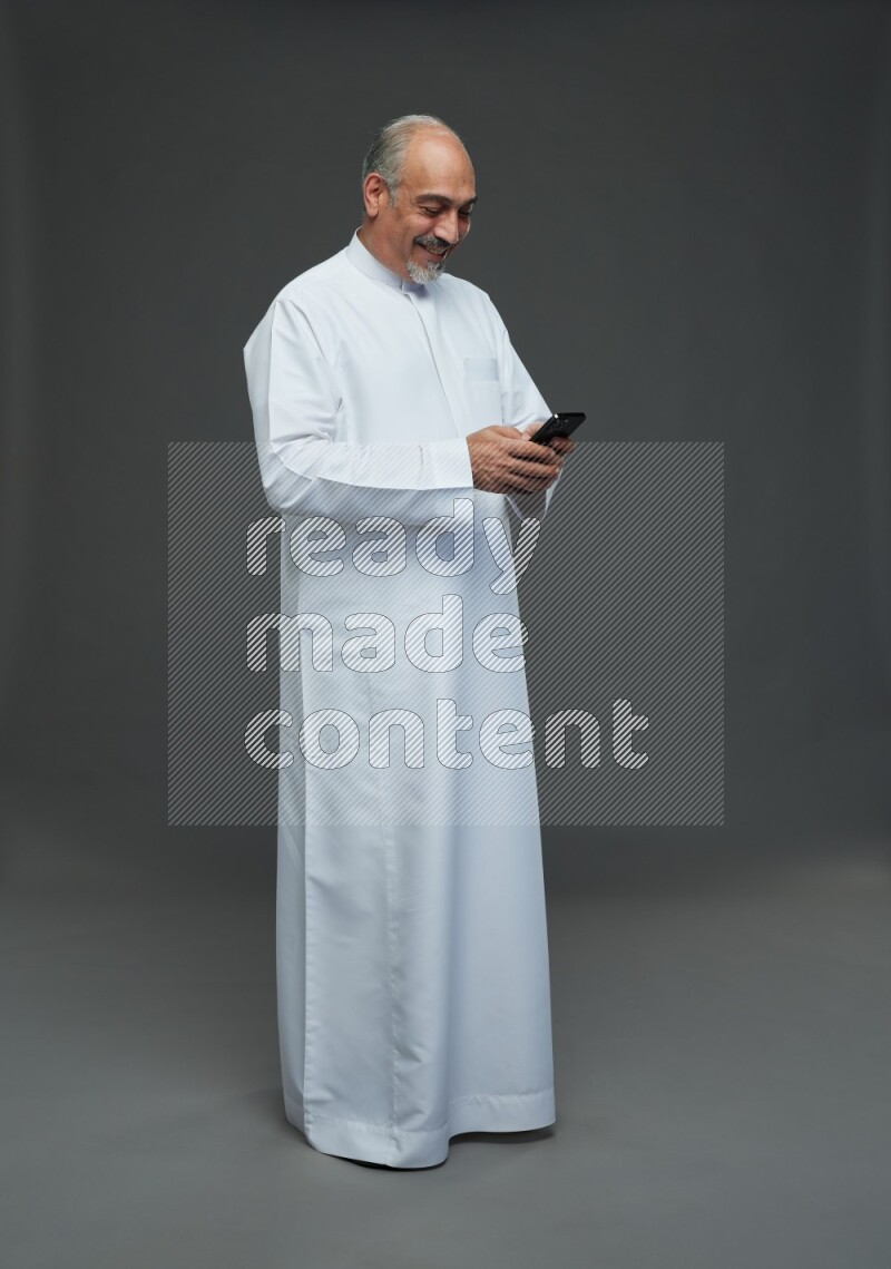 Saudi man without shomag Standing texting on phone on gray background
