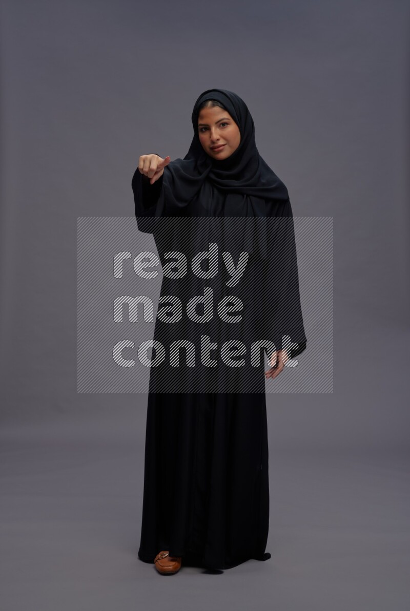 Saudi woman wearing Abaya standing interacting with the camera on gray background