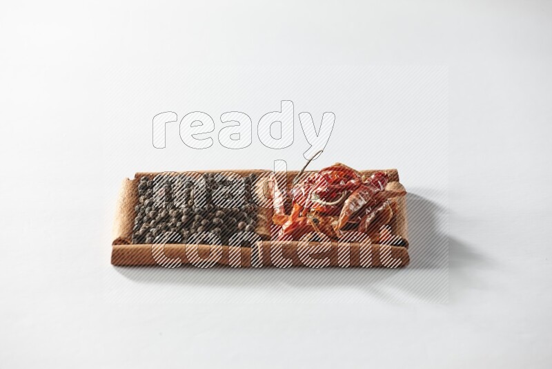 مربعان من أعواد القرفة ممتلئان بالفلفل الحار المجفف وحبوب الفلفل الأسود علي خلفية بيضاء