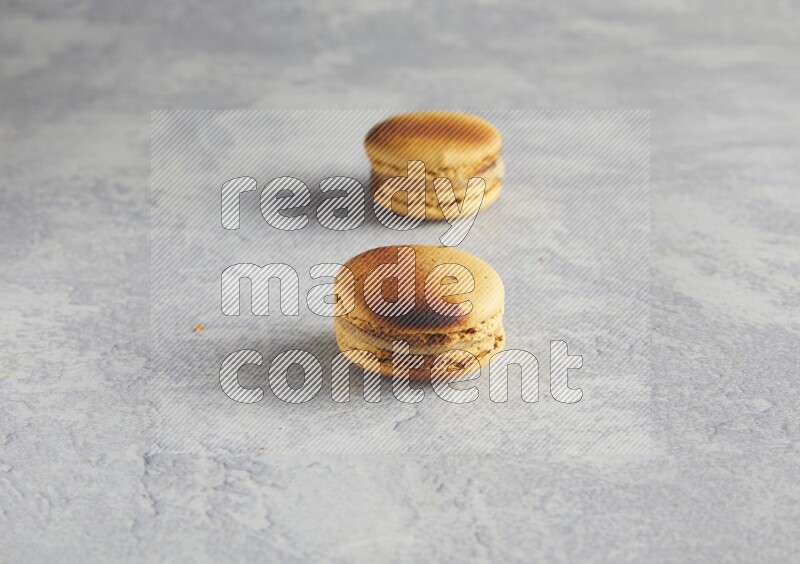 45º Shot of two Yellow Crème Brulée macarons on white  marble background