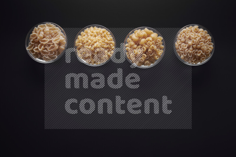 Different pasta types in glass bowls on black background