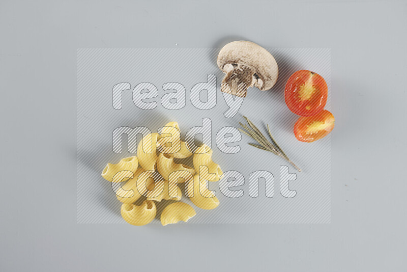 Raw pasta with different ingredients such as cherry tomatoes, garlic, onions, red chilis, black pepper, white pepper, bay laurel leaves, rosemary, cardamom and mushrooms on light blue background