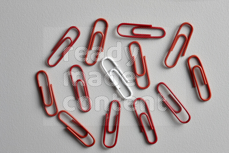A white paperclip surrounded by bunch of red paperclips on grey background