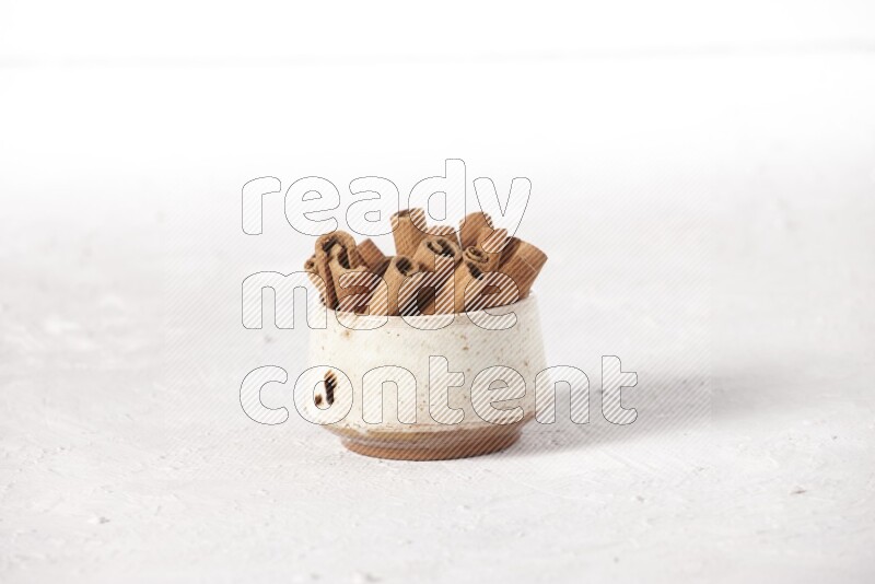 Cinnamon sticks in a beige bowl on a white background