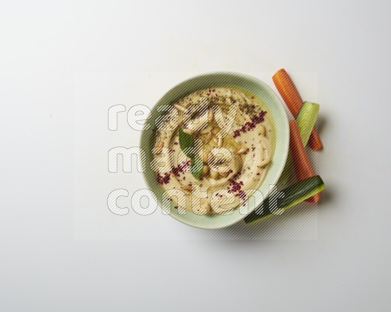 Hummus in a green plate garnished with zattar & sumak on a white background