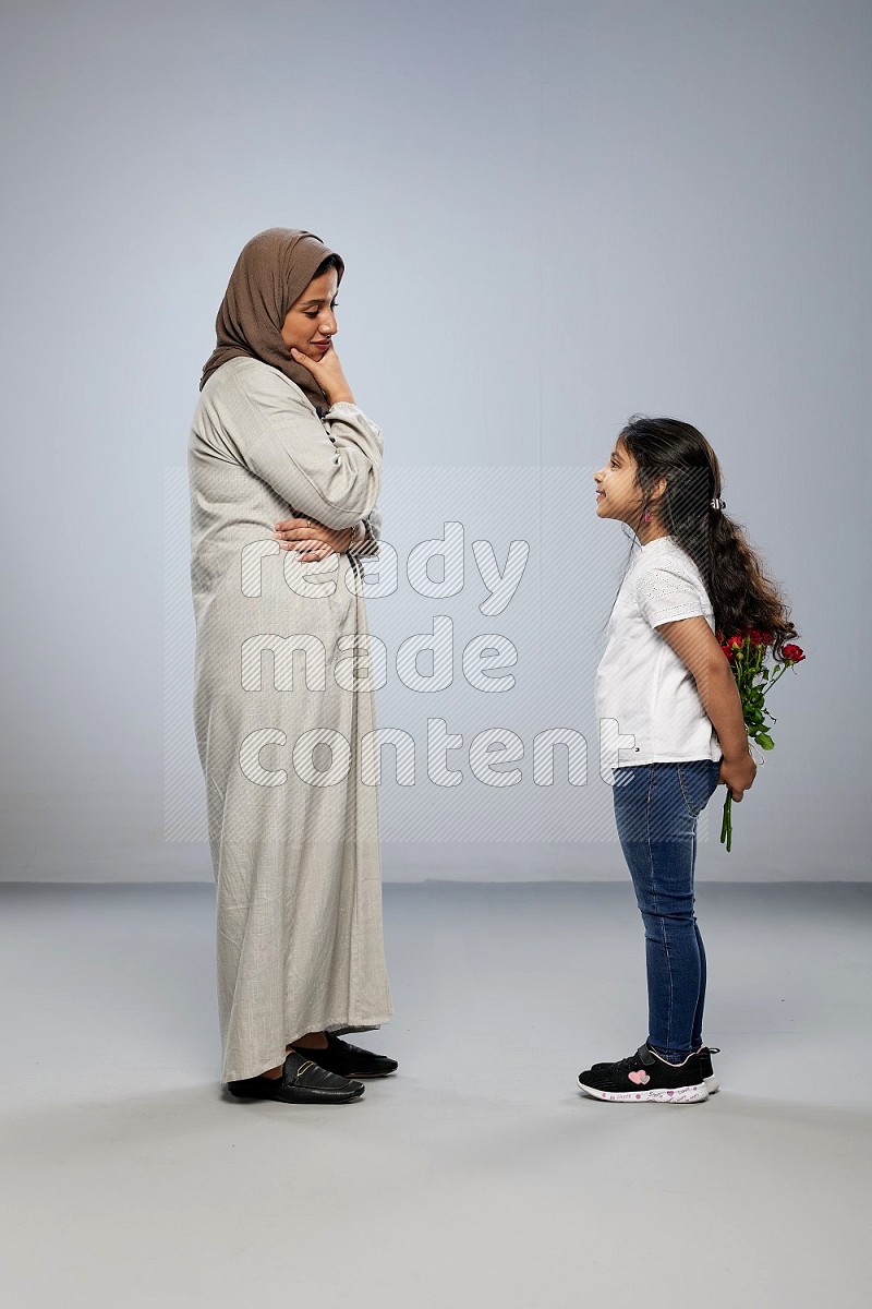 A girl standing giving flowers to her mother on gray background