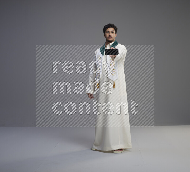 رجل سعودي يرتدي ثوب ابيض و شال يحمل جوال