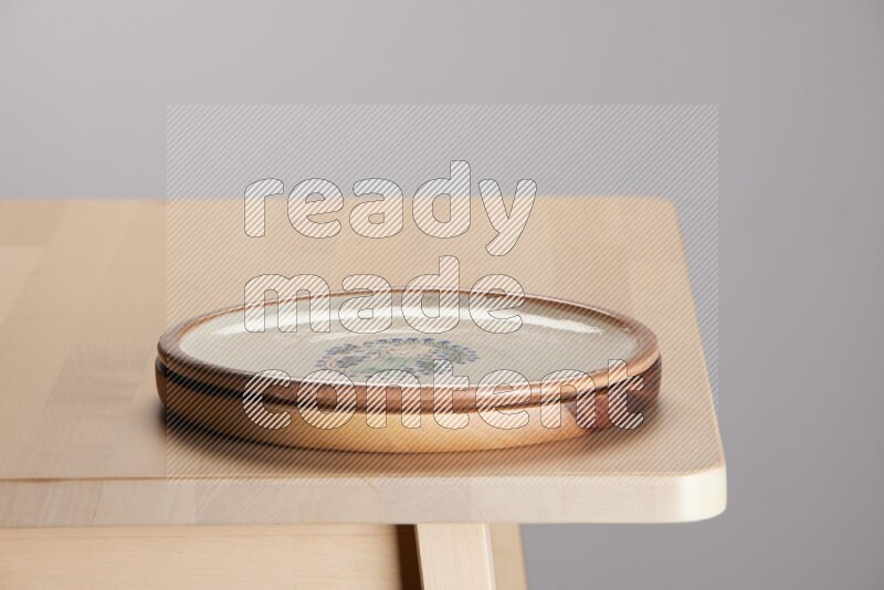 multi-colored pottery Plate placed on a light colored wooden tray on the edge of wooden table
