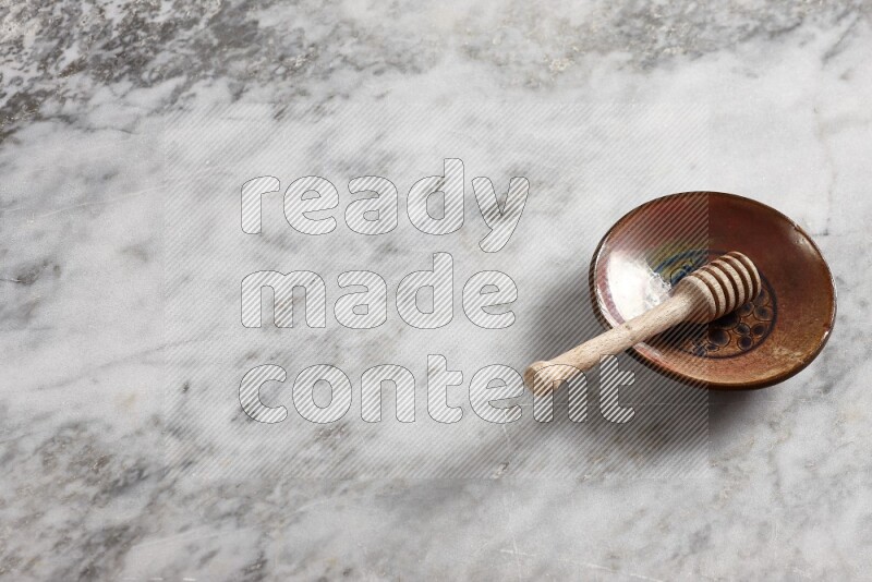 Decorative pottery plate with wooden honey dipper in it on grey marble background