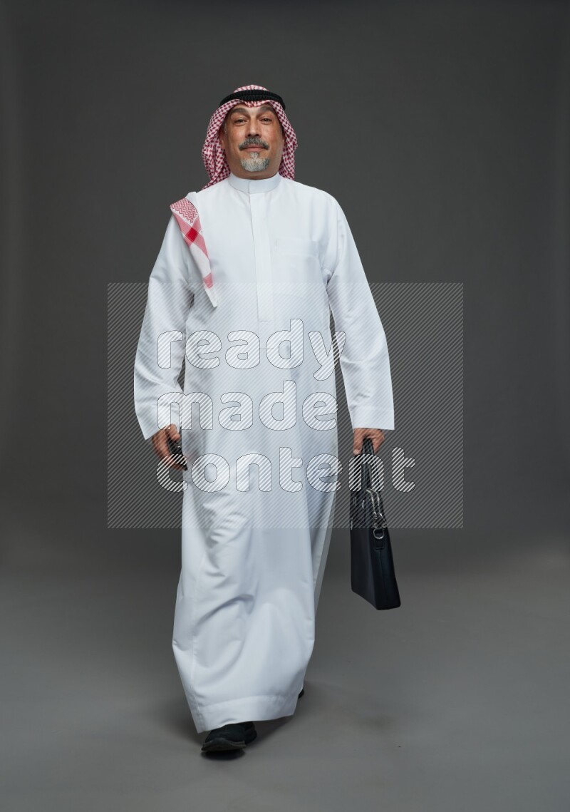 Saudi man with shomag Standing holding bag and phone on gray background