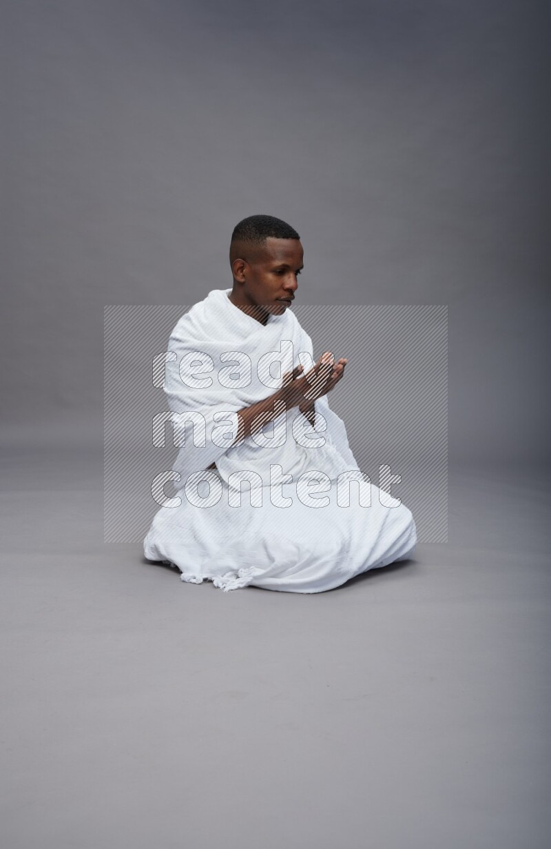 A man wearing Ehram sitting on floor dua'a on gray background