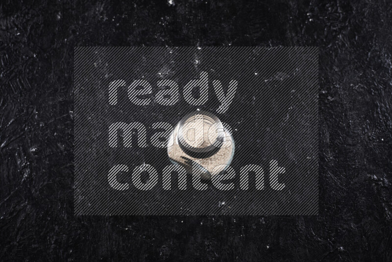 A glass jar full of onion powder on black background