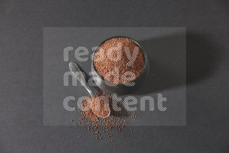 وعاء فخاري أسود ممتلئ ببذور حب الرشاد مع ملعقة معدنية ممتلئة بالبذور على أرضية سوداء