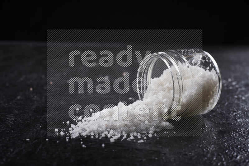 وعاء زجاجي ممتلئ بملح البحر الخشن على خلفية سوداء