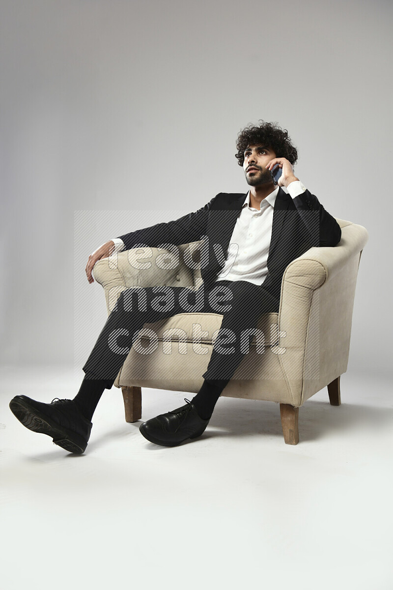 رجل يرتدي ملابس رسمية يجلس علي كرسي و يتحدث في الهاتف علي خلفية بيضاء