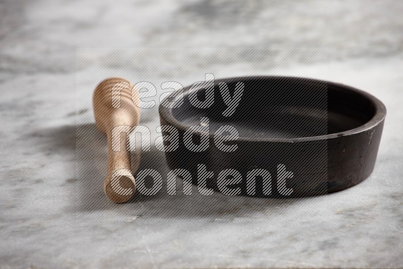 Black Pottery Oven Plate with wooden honey handle on the side with grey marble flooring, 15 degree angle