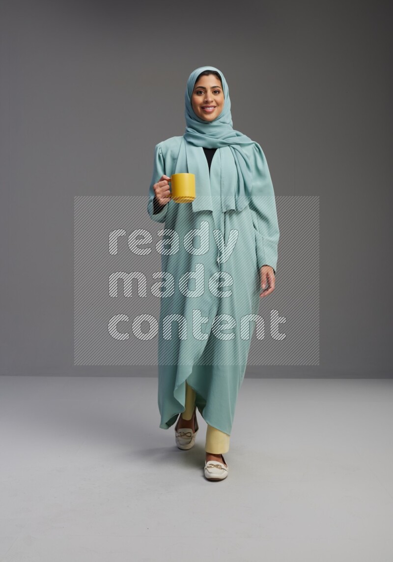 Saudi Woman wearing Abaya standing  holding a mug on Gray background