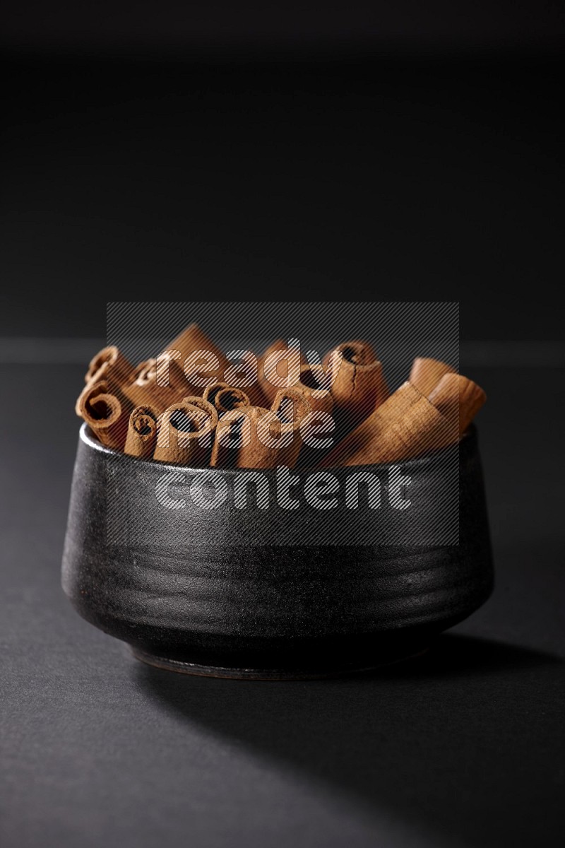 Cinnamon sticks in a black bowl on a black background in different angles