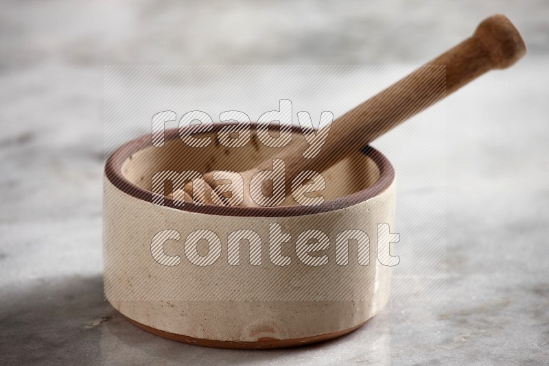 Beige Pottery Oven Bowl with wooden honey handle on the side with grey marble flooring, 15 degree angle