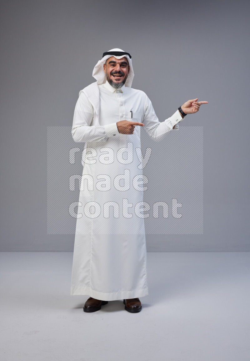 Saudi man Wearing Thob and white Shomag standing interacting with the camera on Gray background